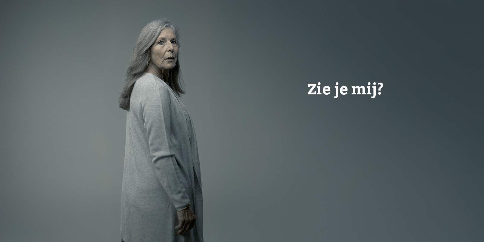 Oudere vrouw met lang grijs haar kijkt bezorgd opzij. Rechts van haar staat de tekst: Zie je mij?