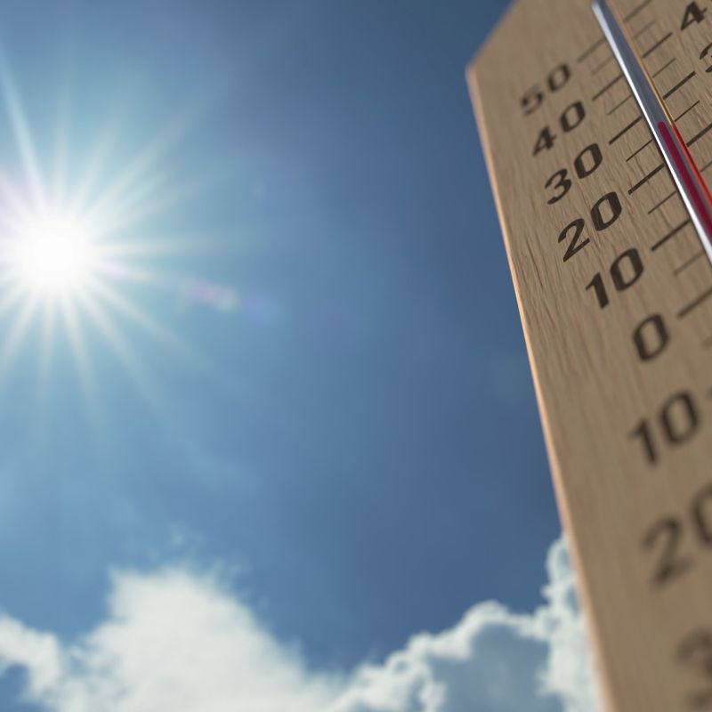 felle zon aan een blauwe hemel met wat wolken een een thermometer die aangeeft dat het rond de 30 graden is.