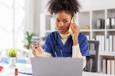 jonge vrouwelijke zorgprofessional aan de telefoon en achter laptop